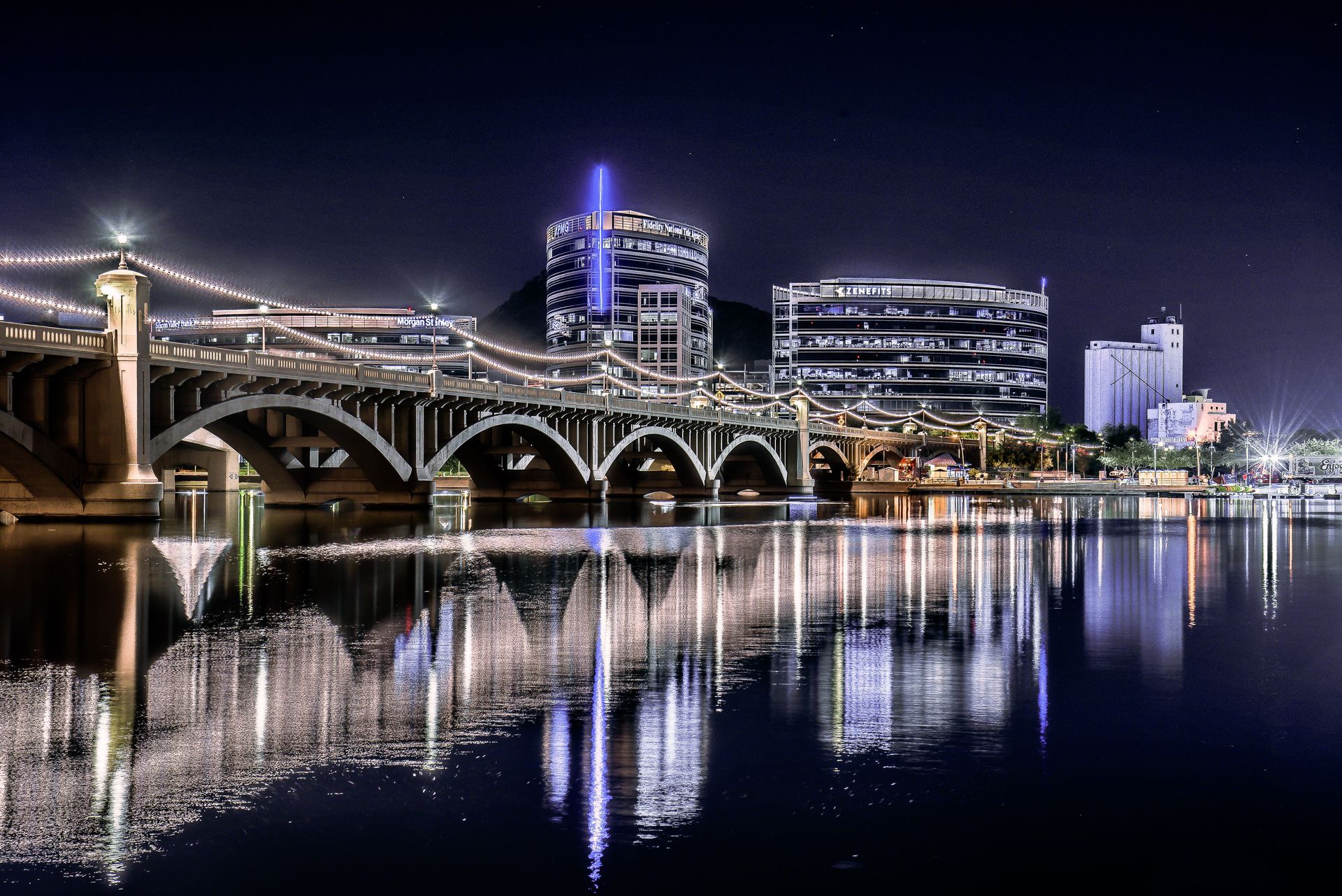 Mill Avenue Bridge and the Tempe Town Lake skyline lit up at night, reflected in the water